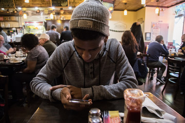 A young man looks at his phone while waiting for his meal © Erik