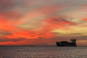 Obraz premium Red container ship arriving from Baltic sea at red sunset sky