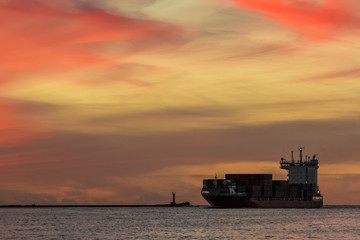 Red container ship arriving from Baltic sea at red sunset sky