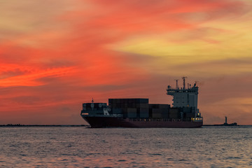 Red container ship arriving from Baltic sea at red sunset sky
