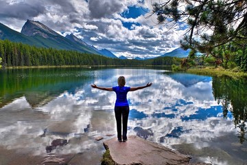 Fototapeta na wymiar Young woman embracing the lake with reflections of clouds and mountains. Honeymoon lake. Banff National Park. Canadian Rockies. Alberta. Canada.