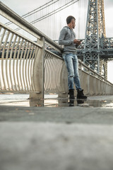 A young man waits along The East River, underneath the Williamsburg Bridge