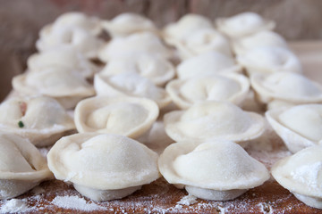 Fototapeta na wymiar Process of making homemade pelmeni (dumplings) on wooden board - traditional dish of Russian cuisine. Selective focus