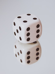 White cubic dice lying on a mirror.