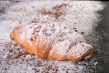 Croissant big and small with chocolate and powdered sugar on black background. French dessert