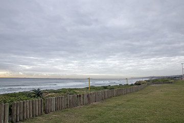 Fototapeta na wymiar Green Lawn and Wooden Pole Barrier Fence on Beachfront
