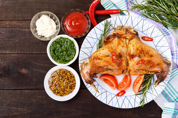 Baked rabbit legs on a plate and different sauces for meat on a dark wooden background. Top view.