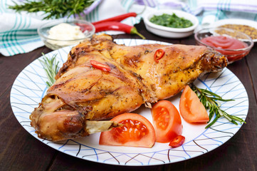 Baked rabbit legs on a plate and different sauces for meat on a dark wooden background.