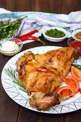 Baked rabbit legs on a plate and different sauces for meat on a dark wooden background.