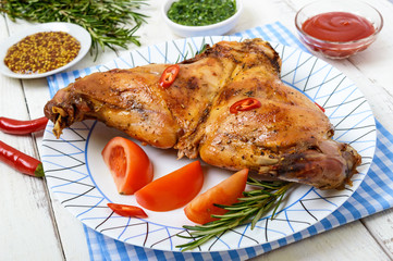 Baked rabbit legs on a plate on a white wooden background.