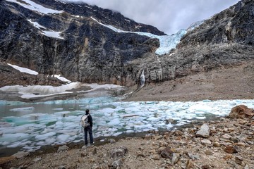 Fototapeta na wymiar Man backpacker by a moraine lake and glacier. Mount Edith Cavell. Angel Glacier. Canadian Rockies. Jasper National Park. Alberta. Canada.