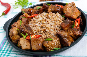 Buckwheat porridge with pieces of fried pork, served on a cast-iron frying pan.