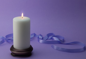 White lit candle with lilac ribbon and background