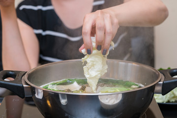 Woman puts vegetables into the pot. Conception of healthy food preparing.