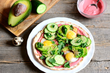 Tortilla with fried quail eggs, avocado, cucumber, beetroot hummus and parsley. Delicious breakfast tortilla on a plate and on vintage wooden table. Healthy breakfast concept