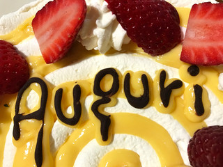 “Auguri” (“best wishes”) written with chocolate on a traditional Italian cake with whipped cream and strawberry for celebrate birthday.