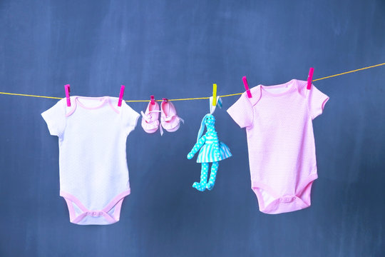 Clothesline with hanging baby clothes and bunny toy on black background