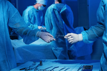 Hands of doctors holding medical instrument and blurred operation on background