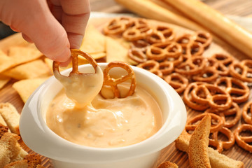 Female hand dipping pretzel in bowl with beer cheese dip, closeup - obrazy, fototapety, plakaty