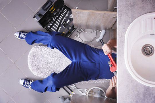 Plumber repairing sink pipes in kitchen