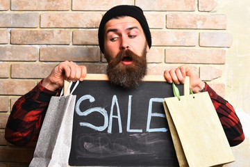 Bearded hipster holding shopping packages and board with Sale inscription