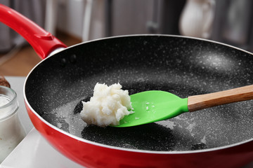 Spoon with coconut oil in frying pan, closeup