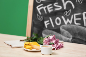 Cup of coffee, tasty cake and beautiful bouquet of flowers on table in cafe