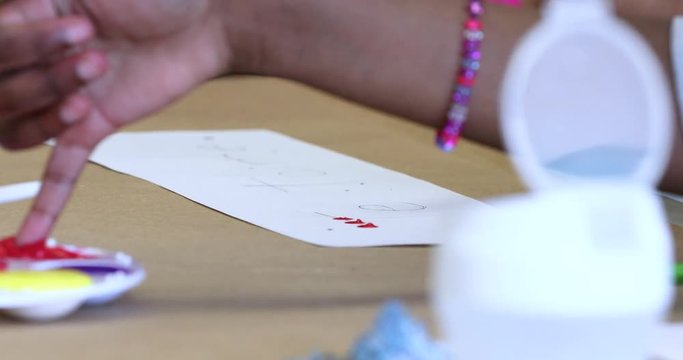 Kid paints letters drawn on a paper with fingers in an close up