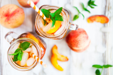 Homemade lemonade with ripe  peaches and fresh mint. Fresh peach ice tea on white wood table. Copy...