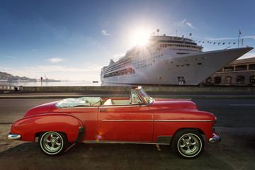 Old car on street of Havana at sunrise with cruise ship in background, Cuba