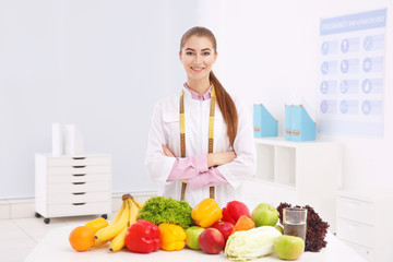 Young female nutritionist with vegetables and fruits in her office