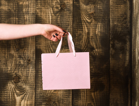 pink shopping bag in female hand on wooden background