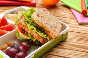 Lunch box with delicious food and stationery on wooden background