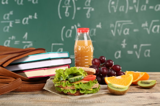 Fototapeta Delicious food, fruits and bottle of juice on wooden table against chalkboard background