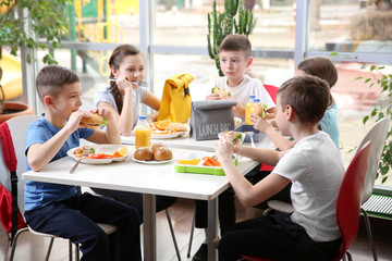 Children sitting at cafeteria table while eating lunch