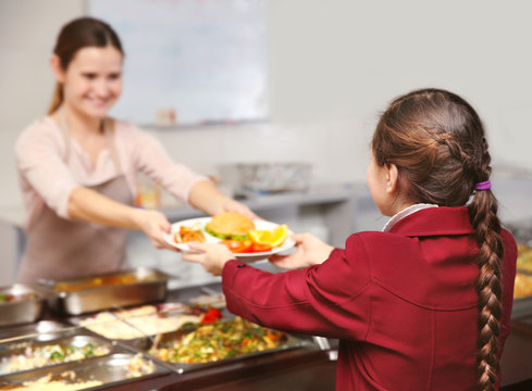 Pleasant woman giving lunch to school girl in cafeteria