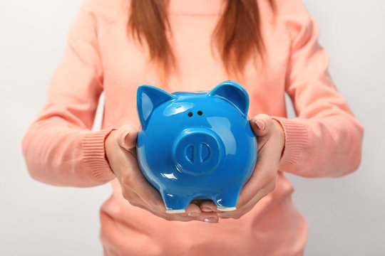 Young woman with piggy bank on light background, closeup
