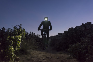 Naklejka premium Cyclist descends the hill at night lit by lantern