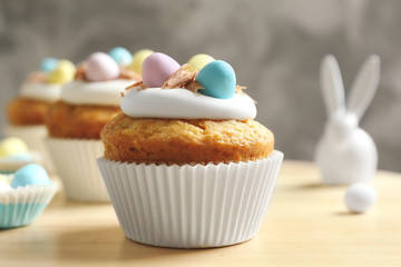 Decorated Easter cupcakes on wooden table against grey background