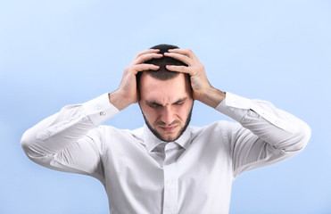 Handsome young man suffering from headache on color background