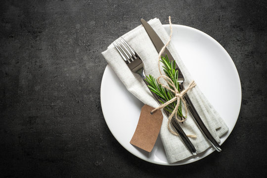 Table setting. Fork knife and white plate at dark slate table.
