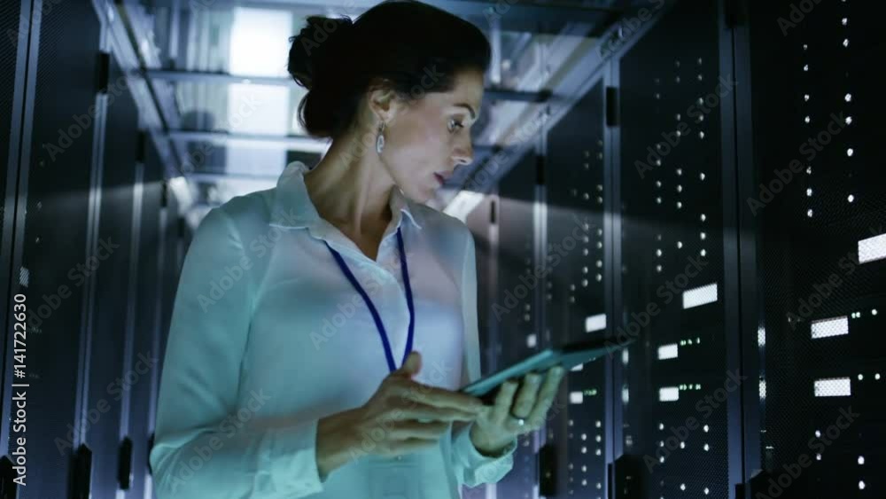Poster female server technician walking in data center corridor with rows of rack servers. she's running di