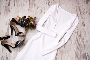 Obraz na płótnie Canvas White dress with a sleeve, shoes, bouquet. Wooden background. Fashionable concept, top view