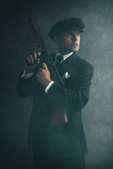 Retro 1920s english gangster wearing flat cap and suit. Standing with gun.