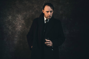 Retro 1920s english gangster holding glass of whiskey. Peaky blinders style.