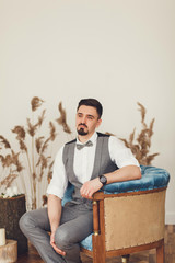 Groom with bow tie sits in a chair