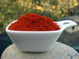 Red chilli powder in white bowl on rounded stone