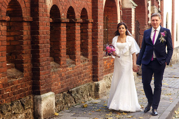 Bride and groom look in each other eyes walking along the street covered with yellow leaves