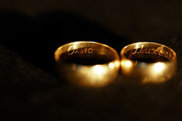 Golden wedding rings with newlyweds names inside lie on black cover