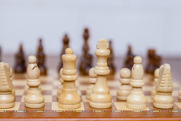 Weiße Schachfiguren auf einem Schachbrett in Ausgangsstellung Blick von hinten. Gegner unscharf